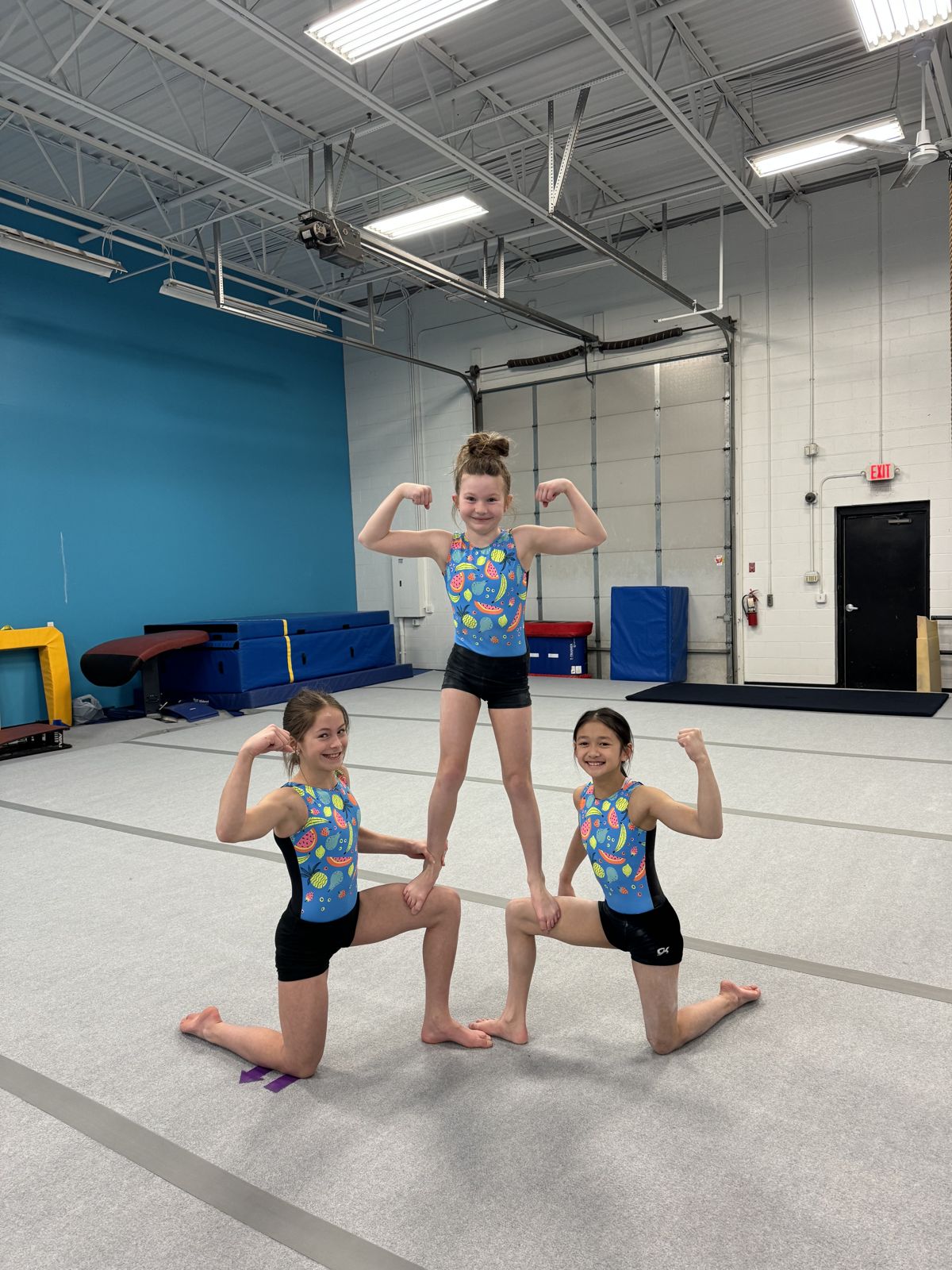 Three gymnasts flexing in a mini pyramid
